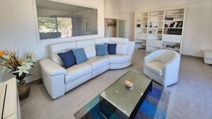 A modern living room with a white sofa, a glass coffee table, and a bookshelf.