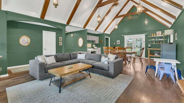 Ein geräumiges Wohnzimmer mit hohen Decken, einem Ecksofa, einem Holztisch und einem Essbereich mit Tisch und Stühlen.
