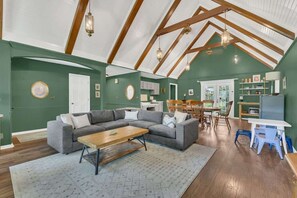 A spacious living room with a high ceiling, a sectional sofa, a wooden coffee table, and a dining area with a table and chairs.
