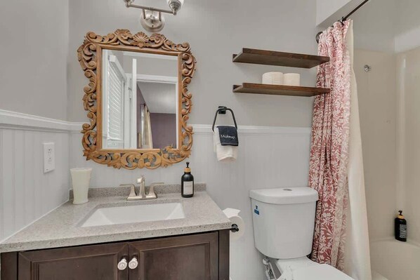 A bathroom with a wooden-framed mirror, a white sink, a toilet, and a shower curtain.