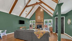 Ein geräumiges Wohnzimmer mit einem großen, grauen Ecksofa, einem Kamin und einer hohen Decke mit freiliegenden Holzbalken.