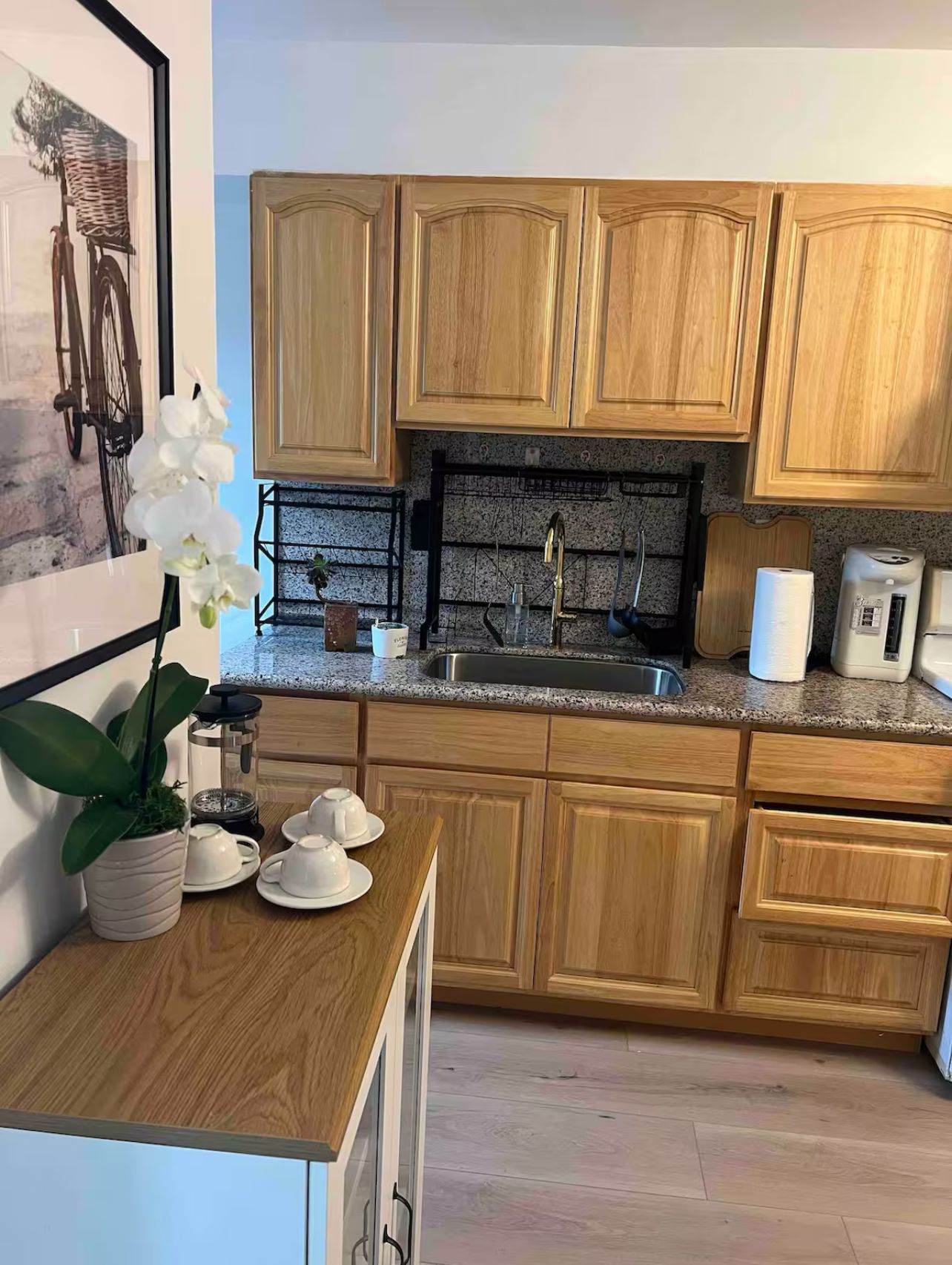 Una cocina con armarios de madera, encimera de granito, pileta y cafetera.