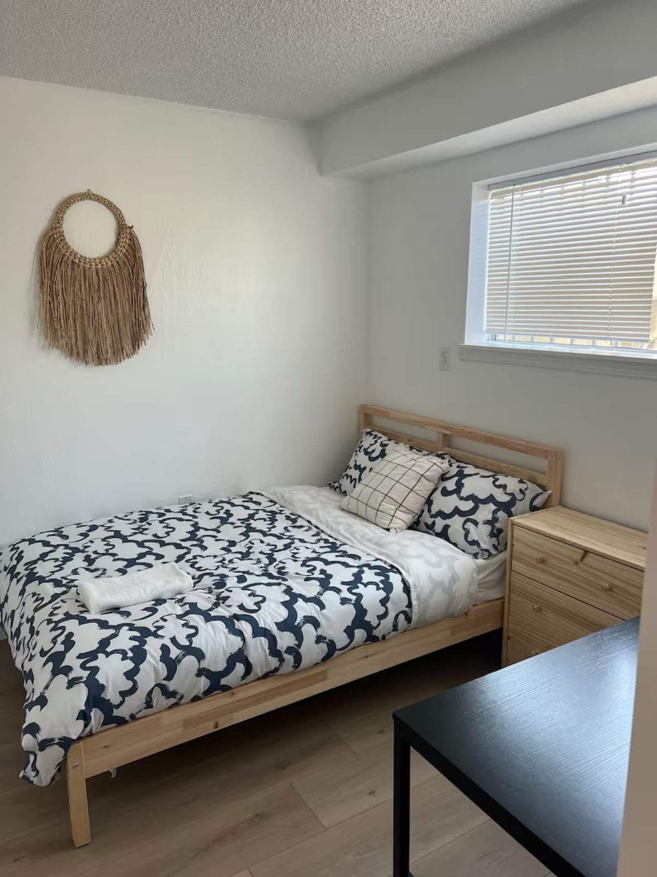Een slaapkamer met een bed, nachtkastje en een macramé decoratie aan de muur.