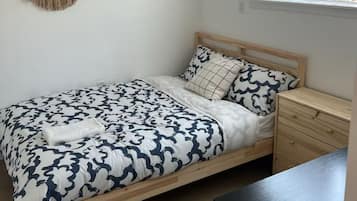 Een slaapkamer met een bed, nachtkastje en een macramé decoratie aan de muur.
