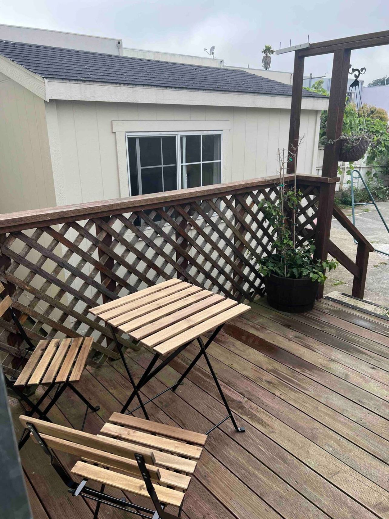 A wooden deck with a metal railing, a potted plant, and a window.