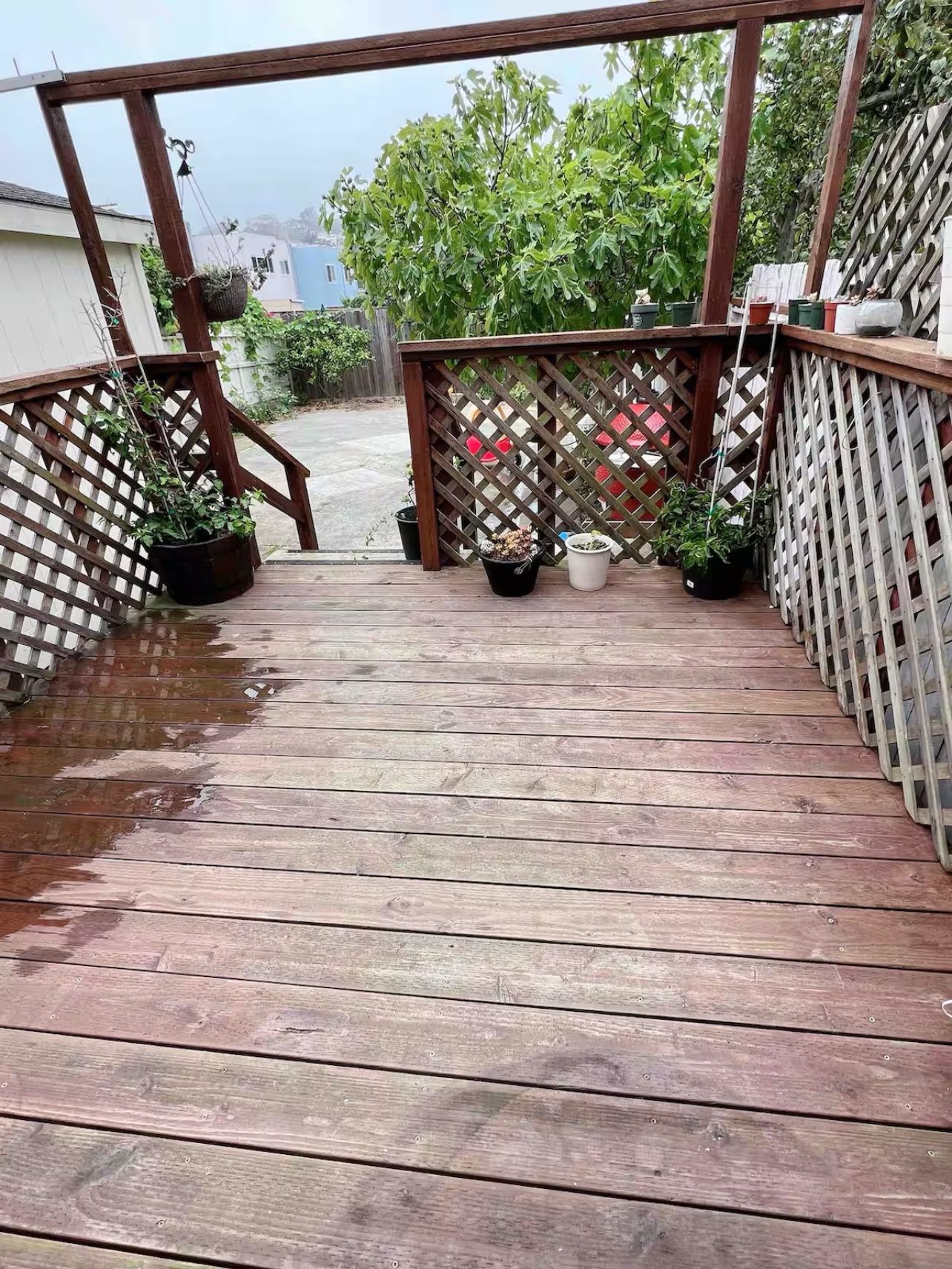 A wooden deck with a lattice railing, potted plants, and a view of a residential area.