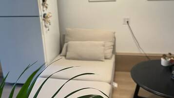 Pieni huone, jossa on sänky, pieni pöytä, jääkaappi ja ruukkukasvi.