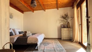Une chambre avec un plafond en bois, un lit recouvert d’un tapis à motifs, une commode et une fenêtre avec des rideaux.