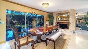 A dining area with a wooden table, chairs, and a bench. There is a fireplace with a mirror above it. The room has a large window and a view of the outdoors. - Swarovski Sanctuary (Key West)