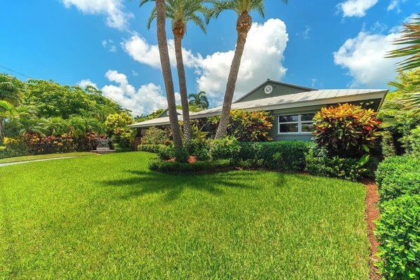 A house with a well-maintained lawn, palm trees, and tropical plants.