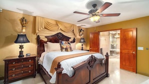 A bedroom with a wooden bed, two bedside tables, a ceiling fan, and a door leading to another room. - Swarovski Sanctuary (Key West)