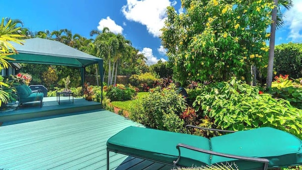 A covered outdoor area with a wooden deck, green lounge chairs, and a variety of tropical plants and trees. - Swarovski Sanctuary (Key West)