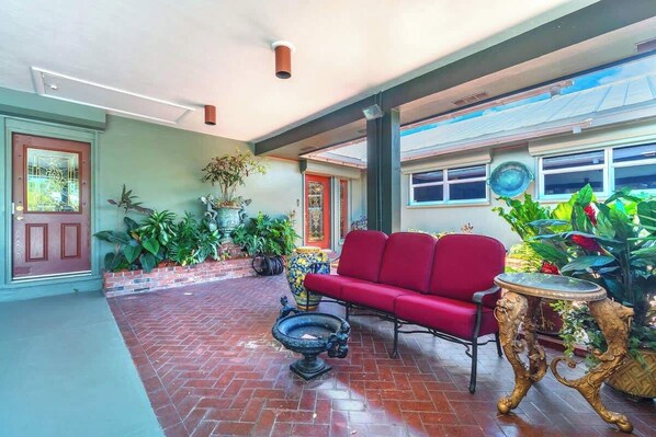 A spacious indoor area with a red sofa, a decorative table, and various potted plants.