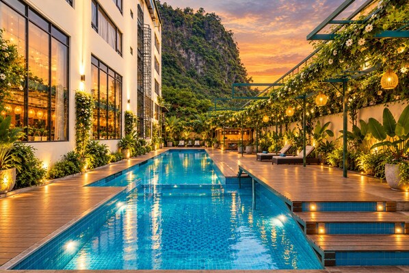 A swimming pool with wooden deck, surrounded by lush greenery and a mountain backdrop.