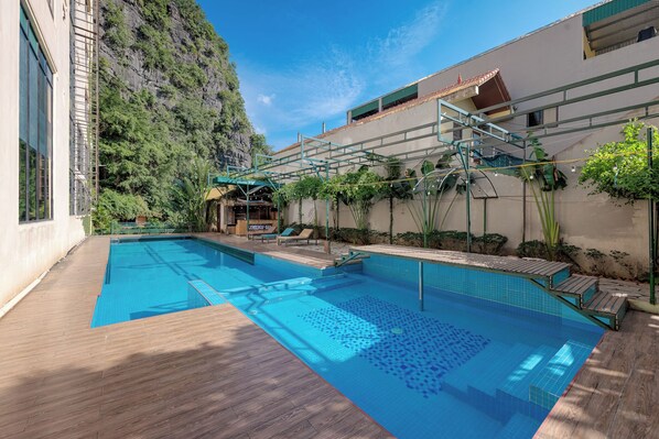 A swimming pool with a wooden deck, a small waterfall feature, and a view of a mountain. - Tam Coc Emerald Retreat (Nam Hoa Lu)