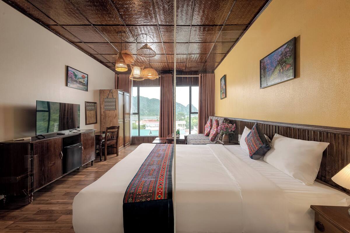 A hotel room with a large bed, a desk with a computer, a TV, and a view of the mountains.