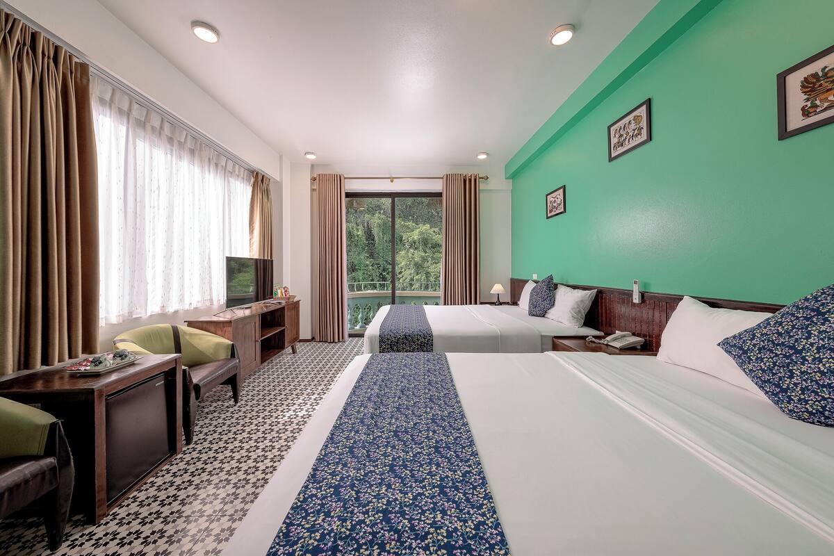 A hotel room with two beds, a desk, a chair, a TV, and a balcony with curtains.