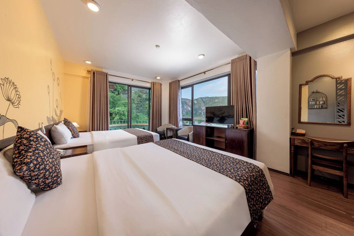A hotel room with two beds, a desk, a television, and a view of the outdoors.