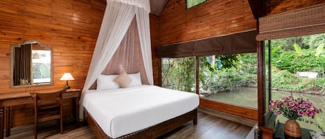 Una habitación de madera con una cama, un escritorio, una silla, un espejo y una ventana con vistas a zonas verdes.