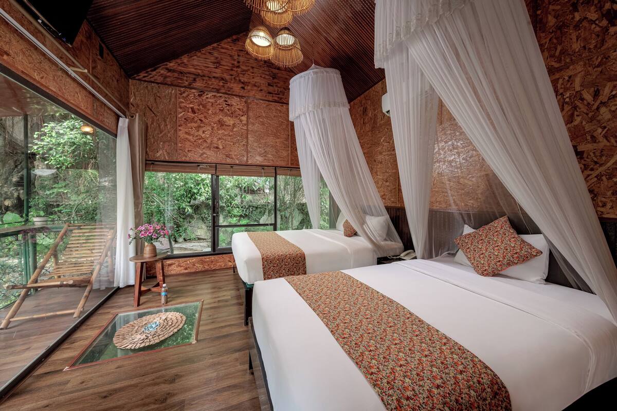 A room with two beds, a glass door leading outside, and a wooden ceiling.