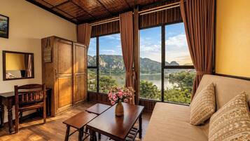 A room with a wooden table, a sofa, and a view of a lake and mountains.