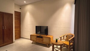 Habitación con una mesita de televisión de madera, un televisor, una pequeña mesa con una planta y dos sillas de madera.