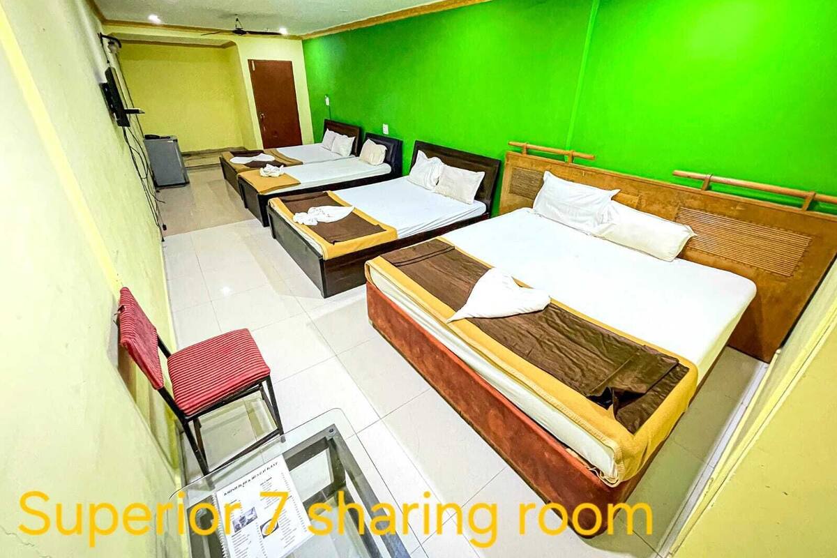 A Superior 7 sharing room with three beds, a small table, and a glass partition.