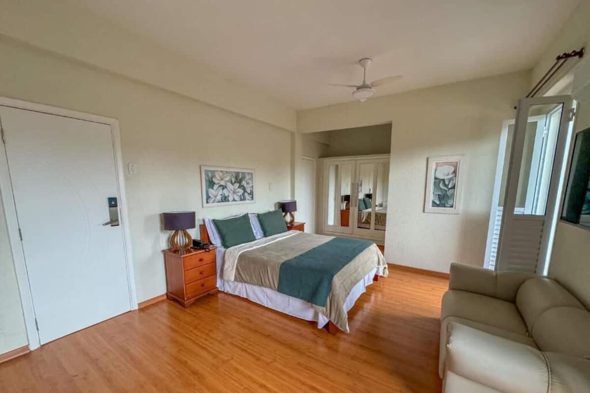 Ein Schlafzimmer mit Bett, Nachttisch, Kommode, Stuhl und Deckenventilator.