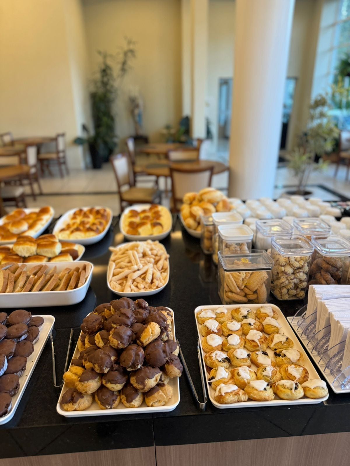 A buffet table with various pastries and desserts, including chocolate-covered items and cream-filled pastries, in a well-lit indoor setting with tables and chairs in the background.