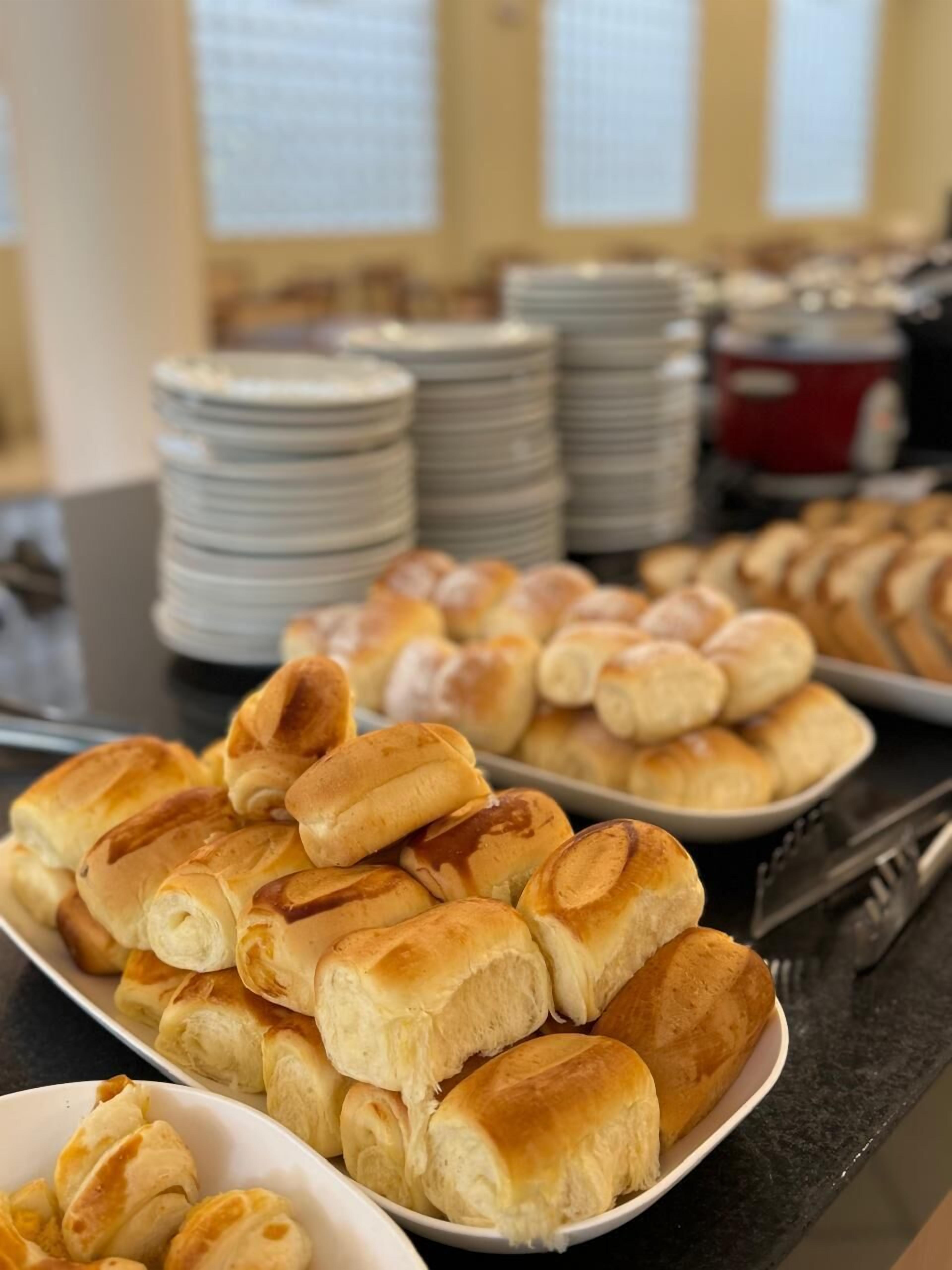 Ein Buffet mit verschiedenen Backwaren, darunter Brötchen und Gebäck, auf Platten und Tabletts angerichtet.