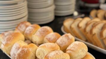 Un tavolo per buffet con diversi prodotti da forno, tra cui panini e dolci, e pile di piatti sullo sfondo.
