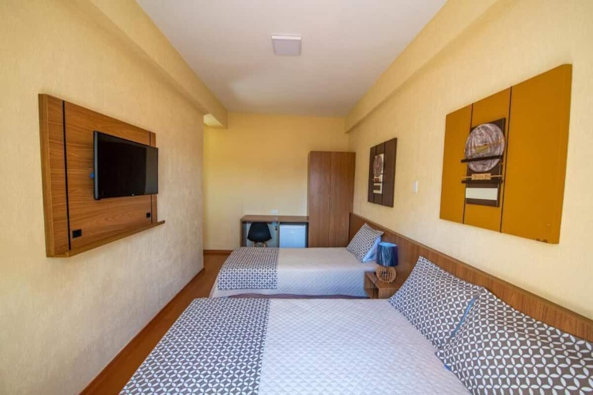 Ein Hotelzimmer mit zwei Betten, einem Fernseher, einem Schreibtisch und einem Kleiderschrank.