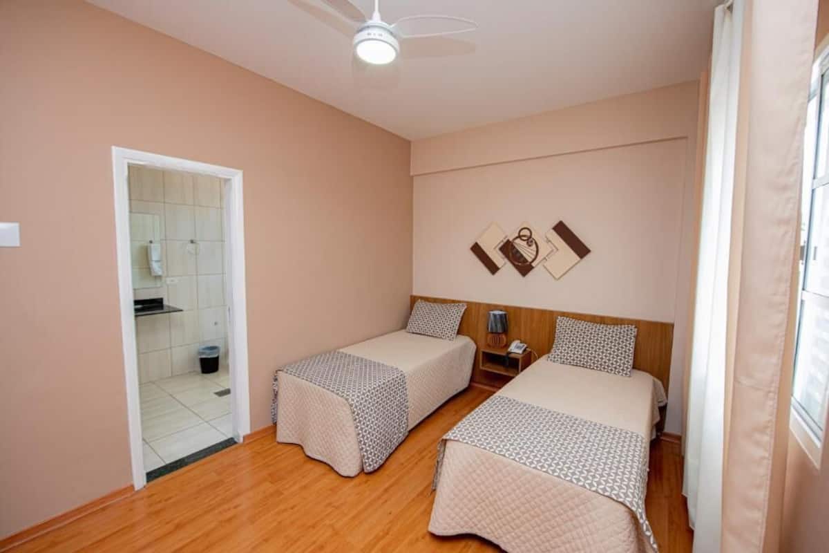 Ein Schlafzimmer mit zwei Einzelbetten, einem Deckenventilator, einem Nachttisch und einem kleinen Fenster.