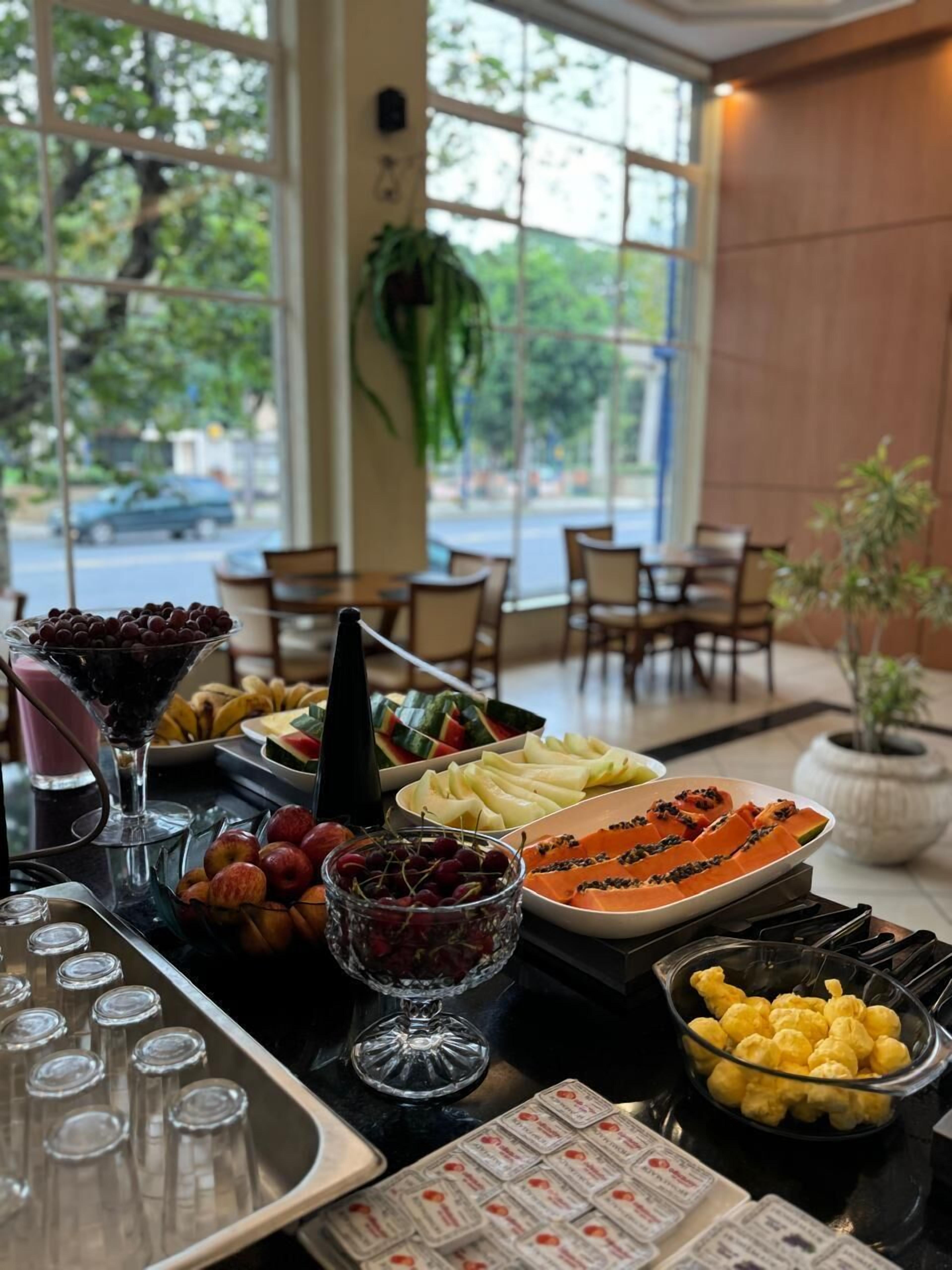 A buffet with various fruits and beverages, a potted plant, and a view of the street outside.