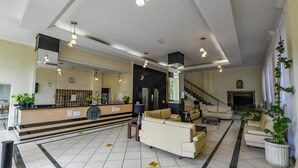 Un hall d’entrée spacieux avec un comptoir d’accueil, plusieurs espaces de détente et un escalier menant aux étages supérieurs.