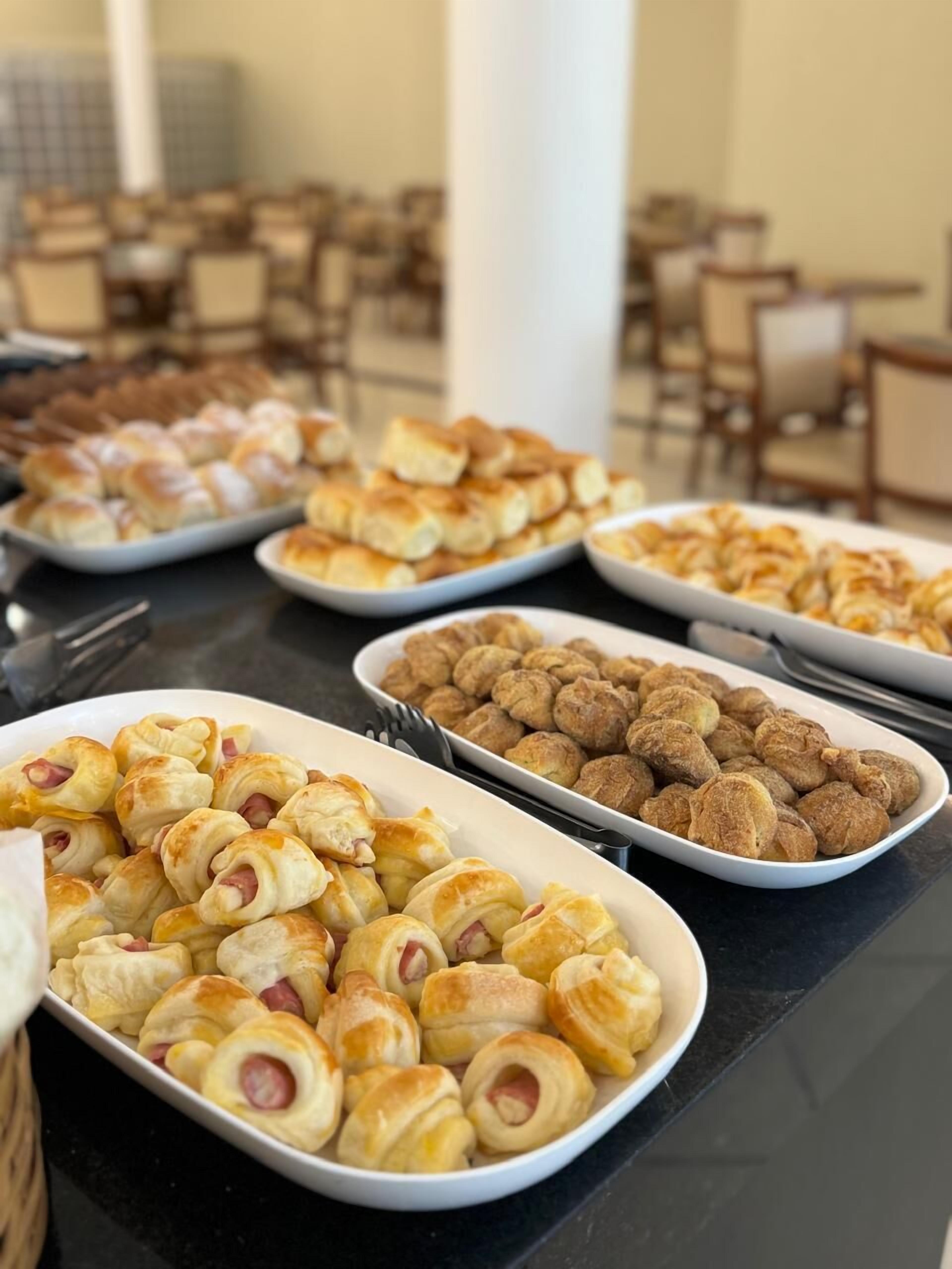 A buffet table with various food items including pastries and rolls.