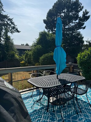 Un patio con una mesa y sillas de metal redondas, una sombrilla azul y una zona de piscina con suelo de diseño azul.