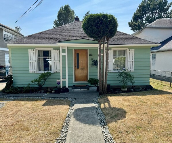Una casa de un piso con fachada verde, contraventanas blancas y el número 133 en la puerta principal.