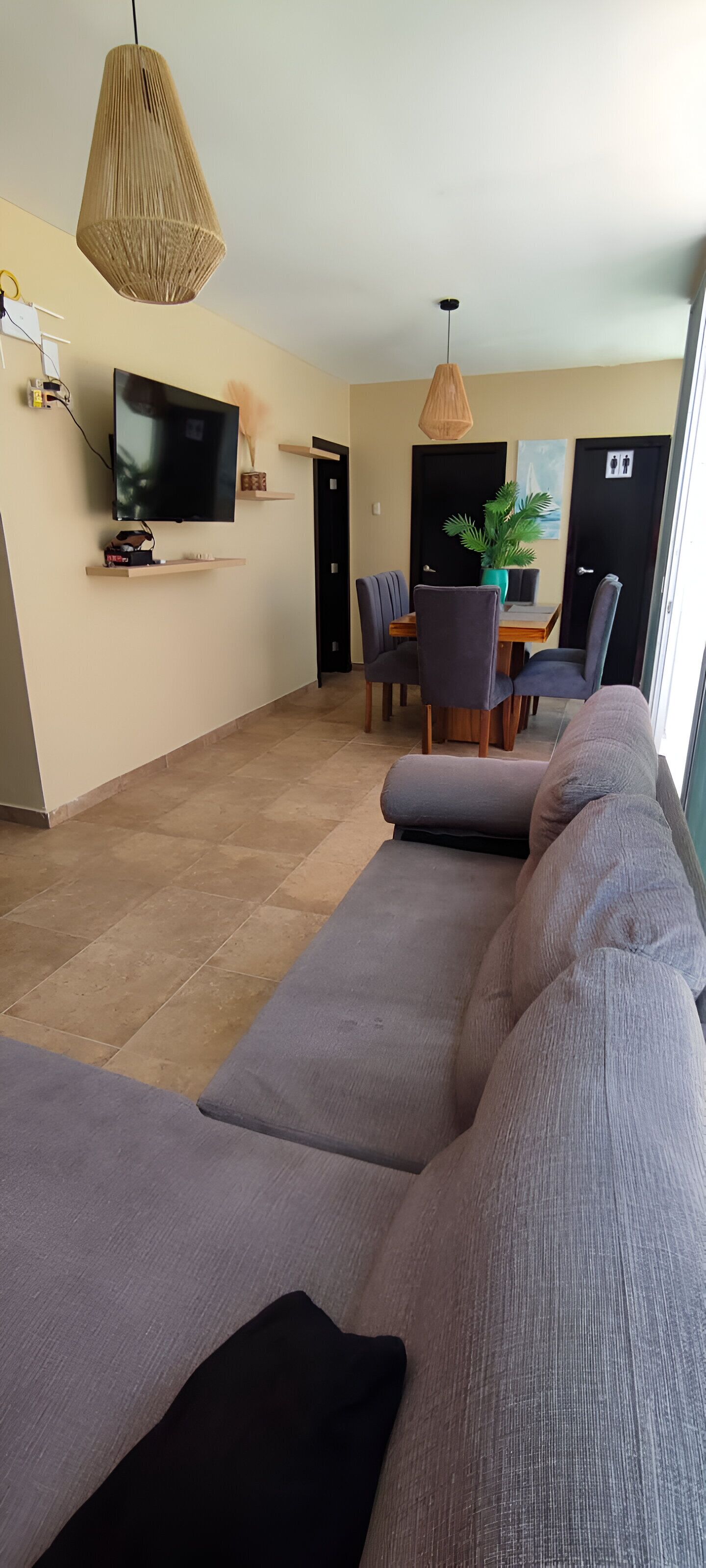 A modern living room with a large gray sofa, a flat-screen TV, and a dining area with a table and chairs.