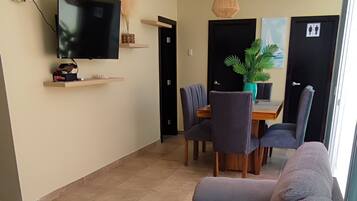 A modern living room with a large gray sofa, a flat-screen TV, and a dining area with a table and chairs.