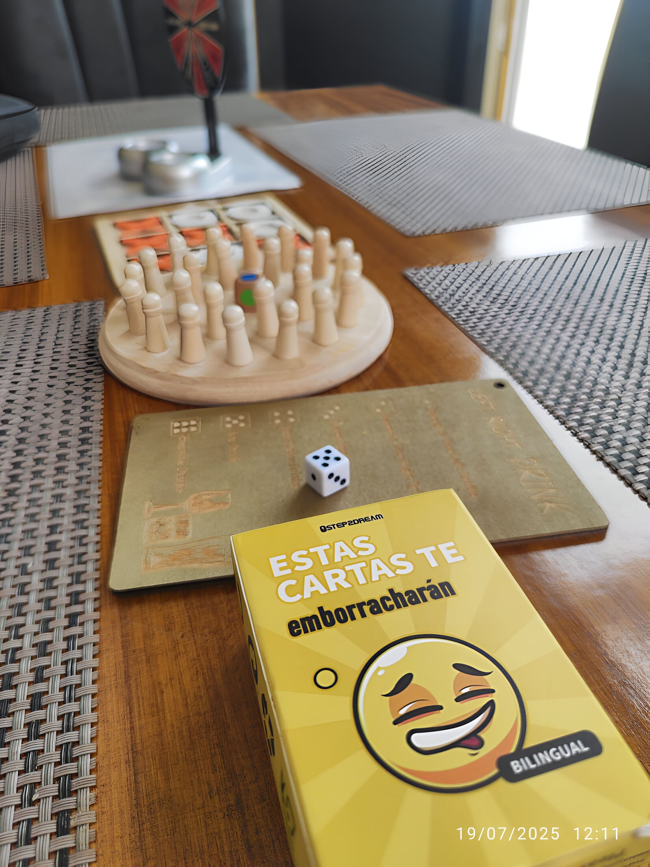 Een houten tafel met een bordspel, dobbelstenen en een doos met een tweetalig kaartspel.