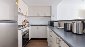 Une cuisine moderne avec des meubles blancs, un plan de travail noir, une cuisinière, un évier et une bouilloire.