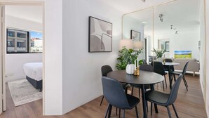 Une chambre d’hôtel moderne, équipée d’un lit, d’un coin repas avec une table et des chaises, et d’un grand miroir qui reflète la pièce.
