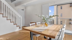 A modern dining area with a wooden table, white chairs, and a vase with greenery. A staircase with wooden steps is visible to the left.