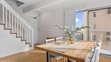 A modern dining area with a wooden table, white chairs, and a vase with greenery. A staircase with wooden steps is visible to the left.