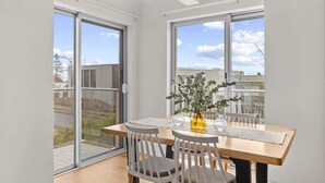 A dining area with a wooden table and chairs, a vase with flowers, and large windows offering a view of the city.