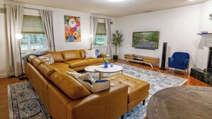 A living room with a sectional sofa, a coffee table, a blue armchair, a fireplace, and artwork on the walls.