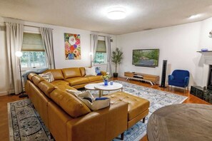 A living room with a sectional sofa, a coffee table, a blue armchair, a fireplace, and artwork on the walls.