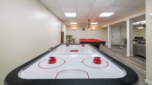 A room with a shuffleboard table, a pool table, and a bar area.