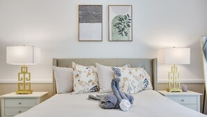 A neatly made bed with floral pillows, a gray plush toy, and two bedside tables with lamps.